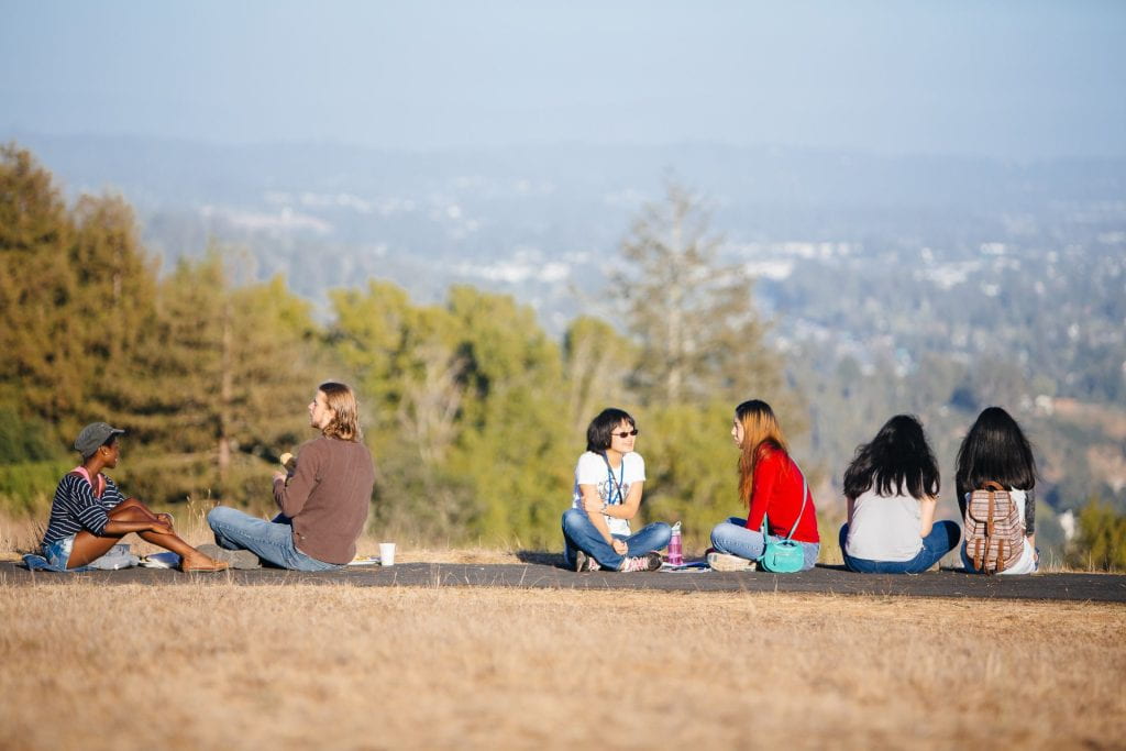 Students sitting on the ground with trees in the background