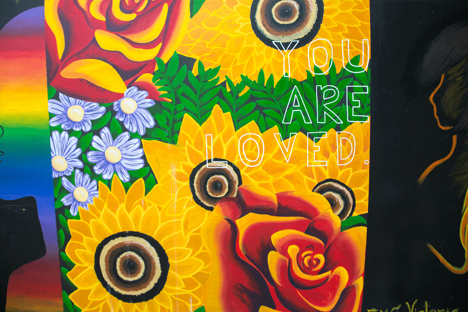 Mural with flowers and a face in rainbow colors, with the words "you are loved."