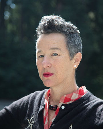 Pale skinned woman with short dark hair (some gray on sides), wearing a red & white checked shirt, and a black cardigan.